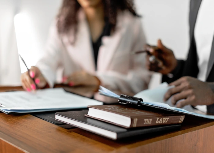 Two people at a desk, one writing with a pen while the other reads a book on trust administration.